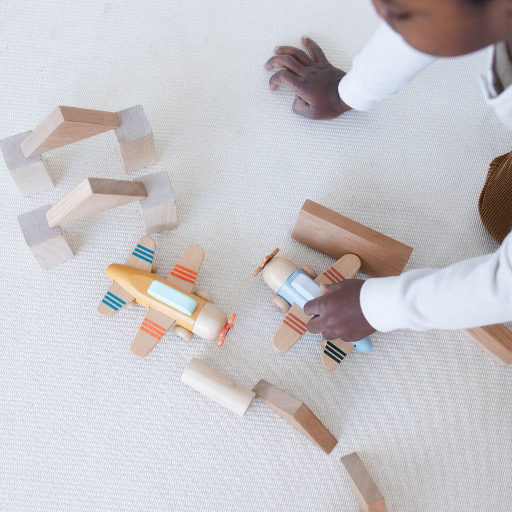 Child playing with wooden building blocks and airplanes on a light surface