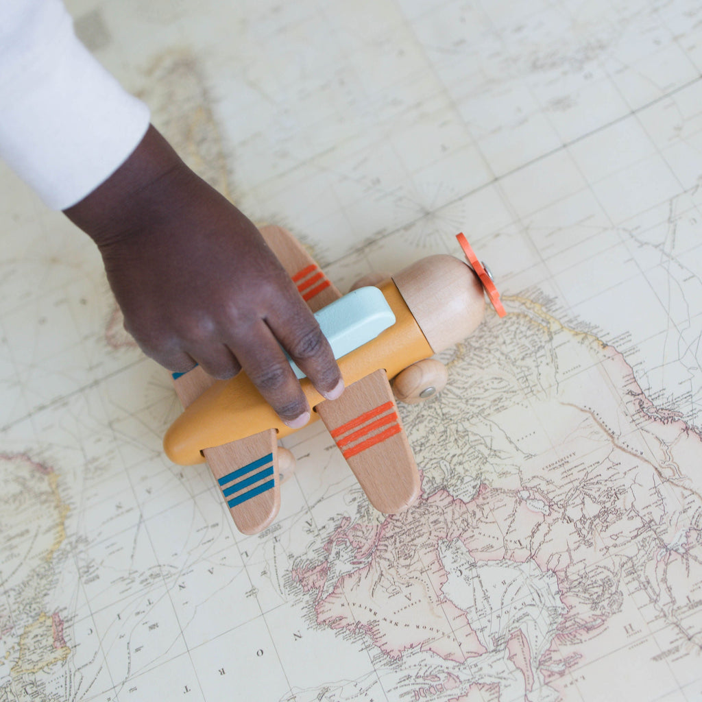 Child's hand holding a toy airplane on a world map