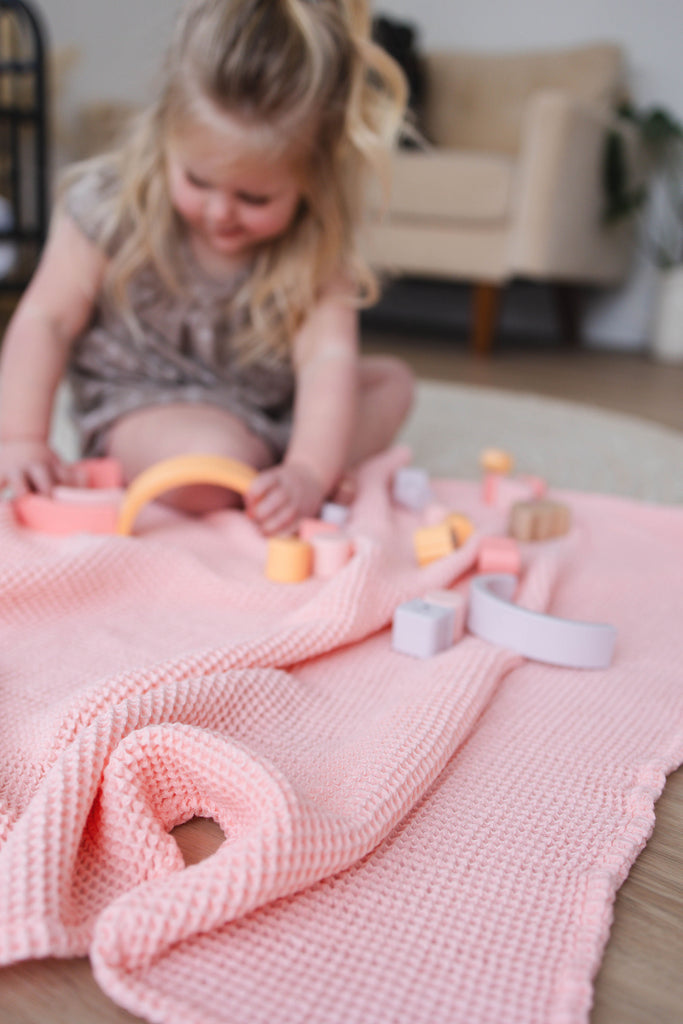 Child playing with toys on a pink blanket in a cozy living room.