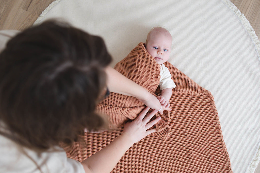 Baby wrapped in a brown blanket with a person holding the blanket