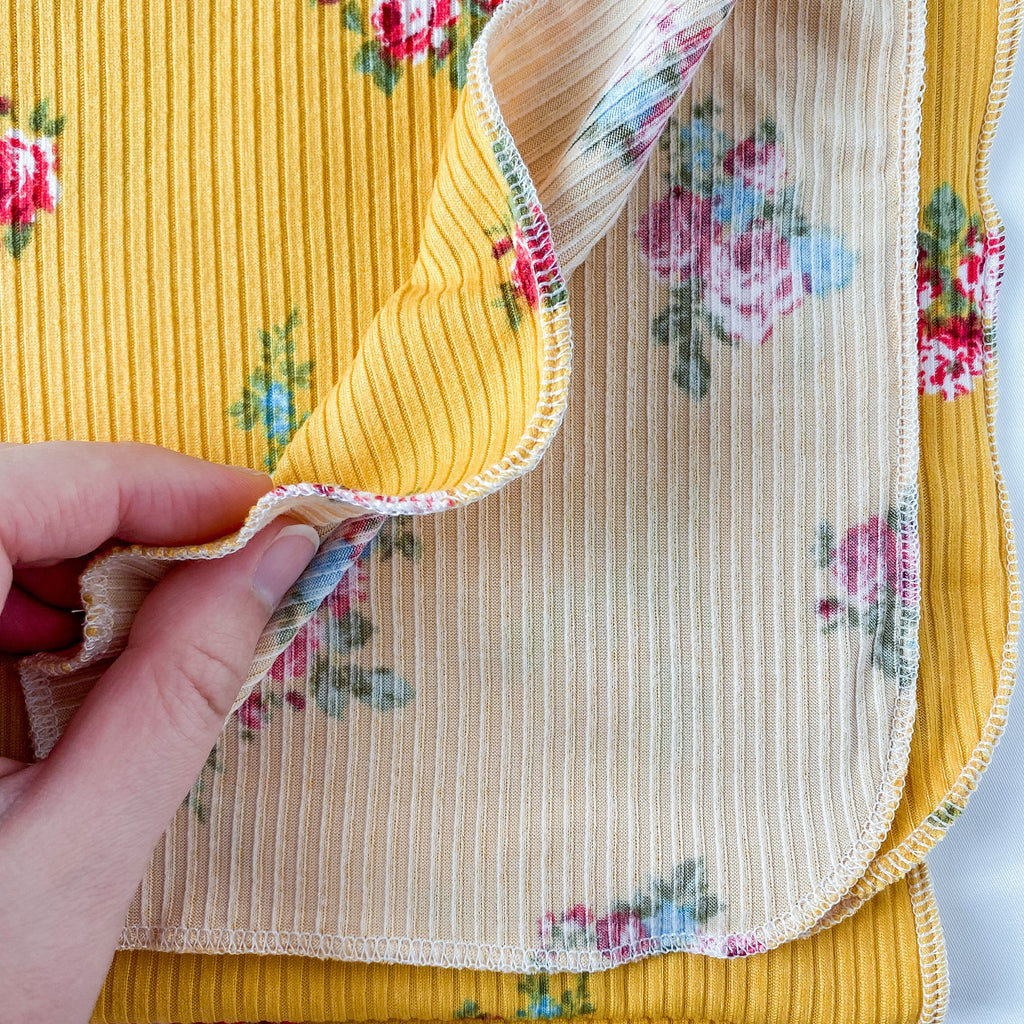 Hand holding a folded fabric with floral patterns on a yellow background